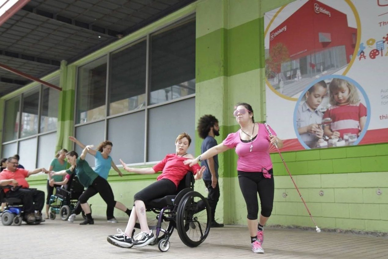 two dancers performing outside. One performer is a sit-down dancer and the other performer is using a guide cane.