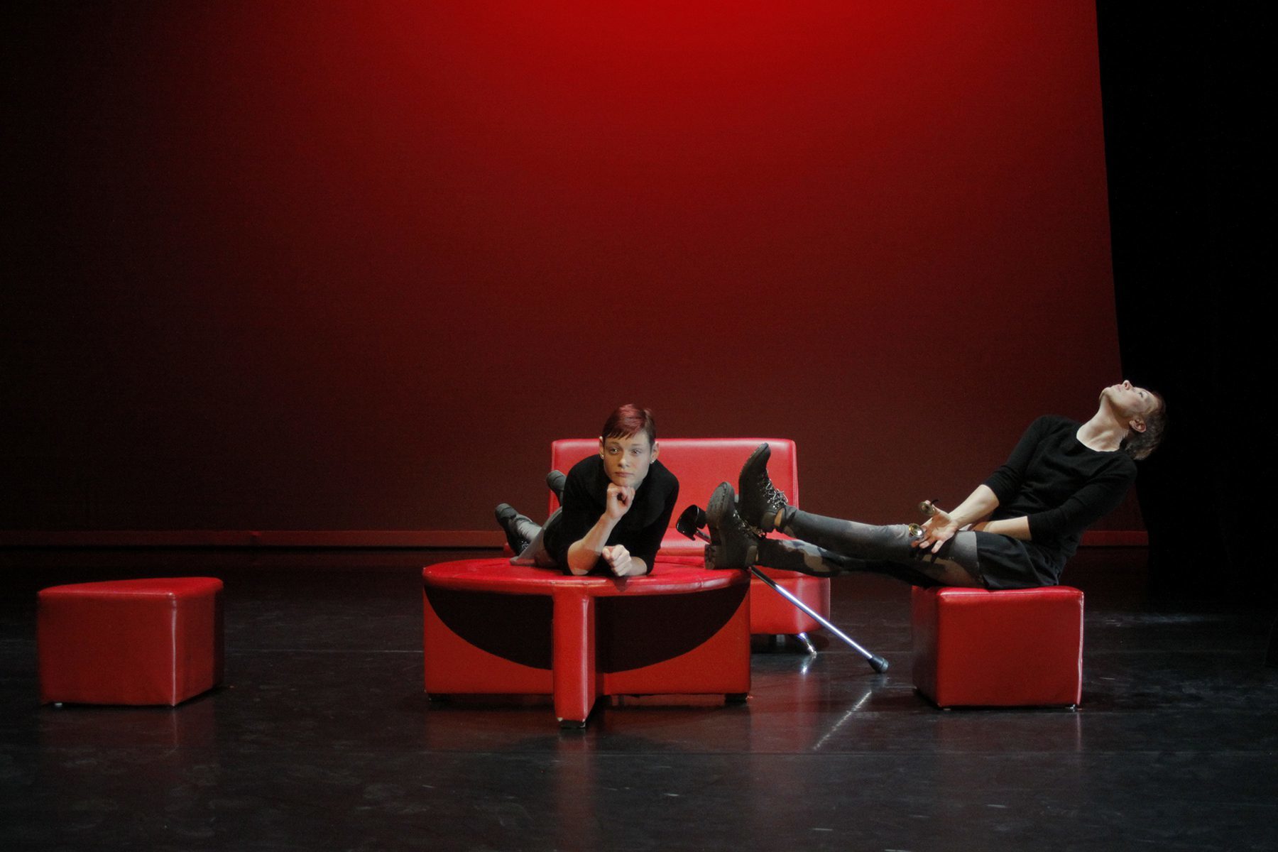 two dancers with and without disabilities perform on stage with red furniture.