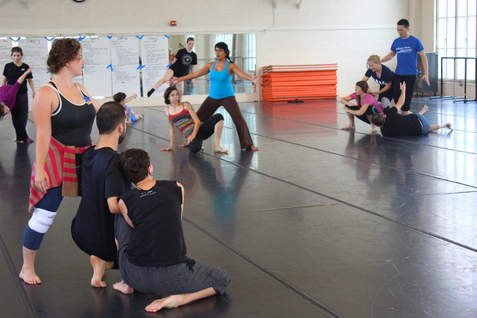 A group of dancers watch as an instructor demonstrates movement.