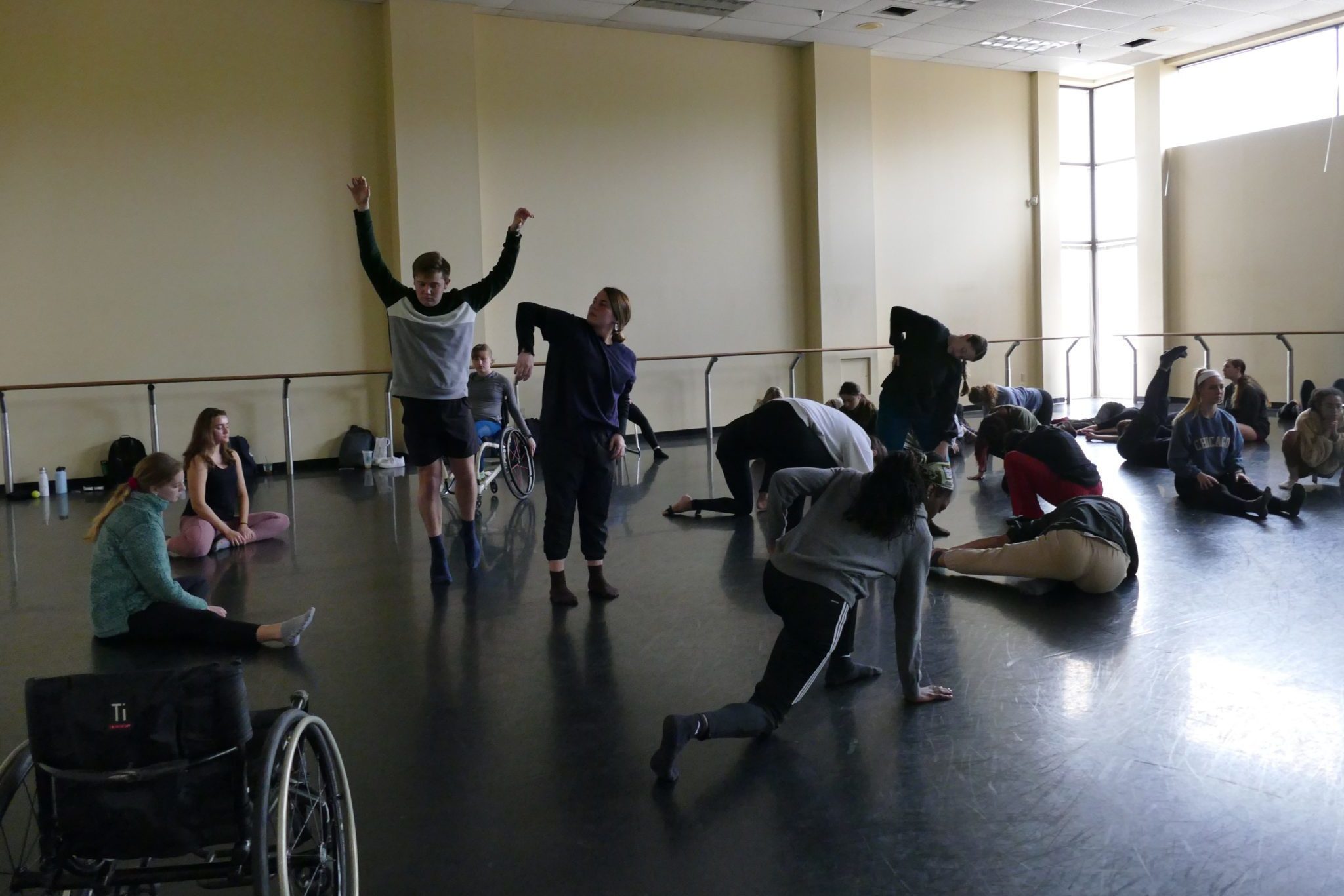 A group of 20 dancers with and without disabilities practice in a dimply lit studio space.