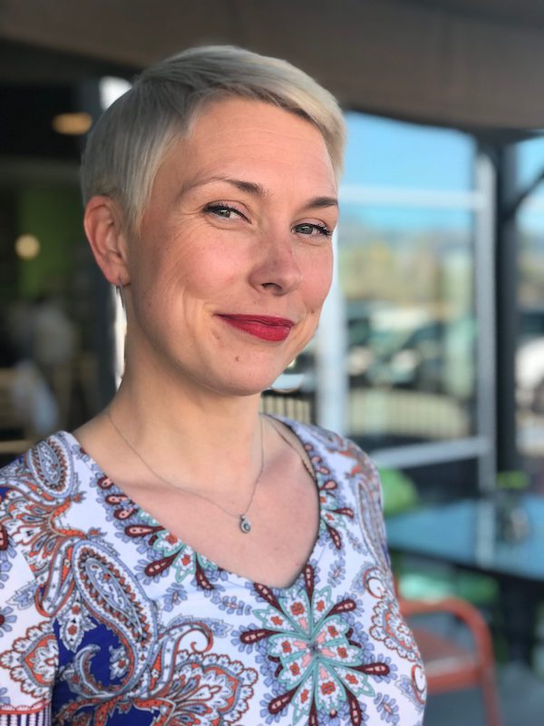 Headshot of Silva Laukkanen smiling standing in front of large glass windows.