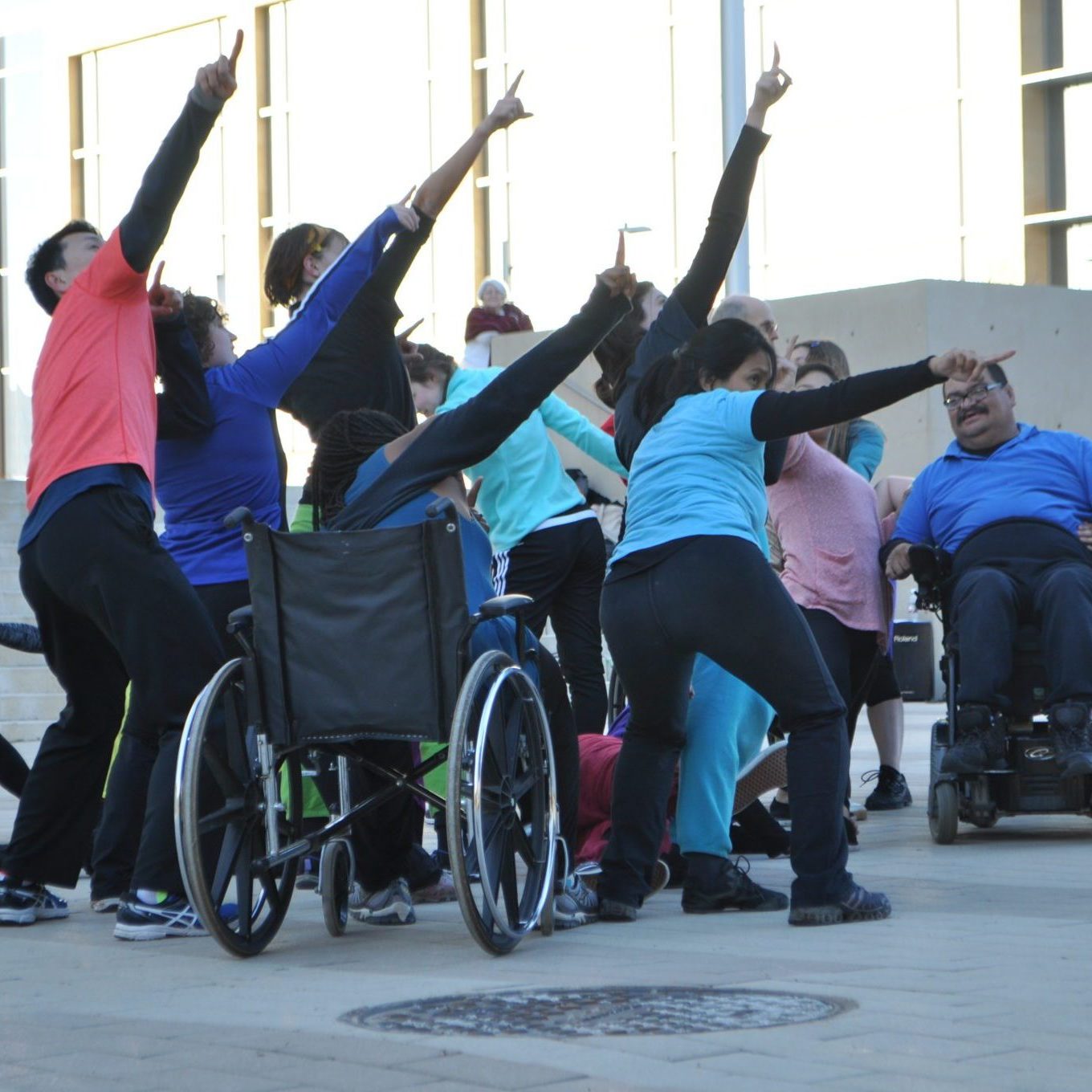 A group of seven dancers with and without disabilities stand pointing to the sky.